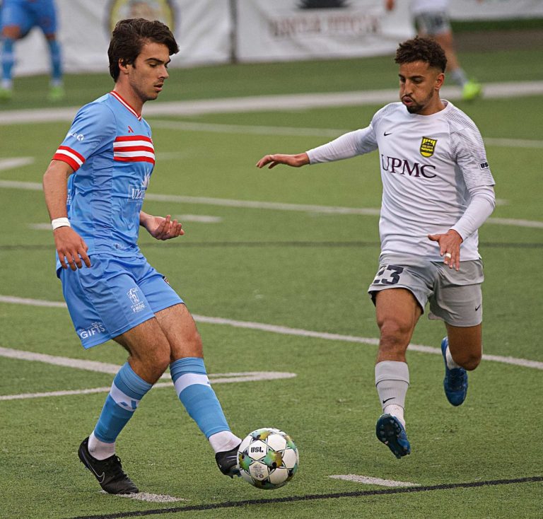 ACFC player in blue uniform controlling soccer ball in front of Steel City player in white uniform