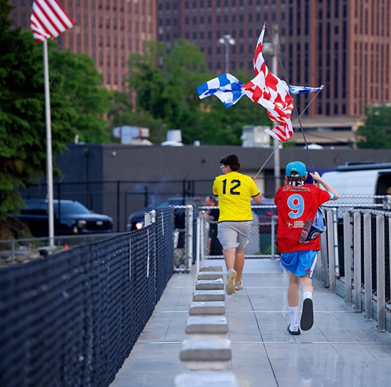 Two boys carrying running down bleachers with red and blue flags